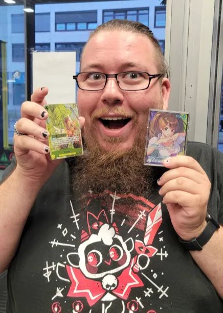 man with glasses and long chinbeard holds up two one piece TCG cards. One is a Winner Card, the other the leader he played.