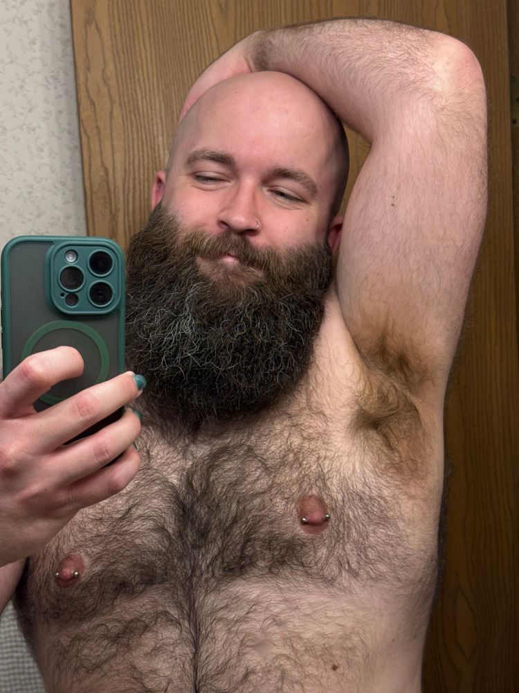 A selfie of me in a mirror. I'm shirtless and bald with a big dark brown beard. My left hand is on my head so you can see my armpit.