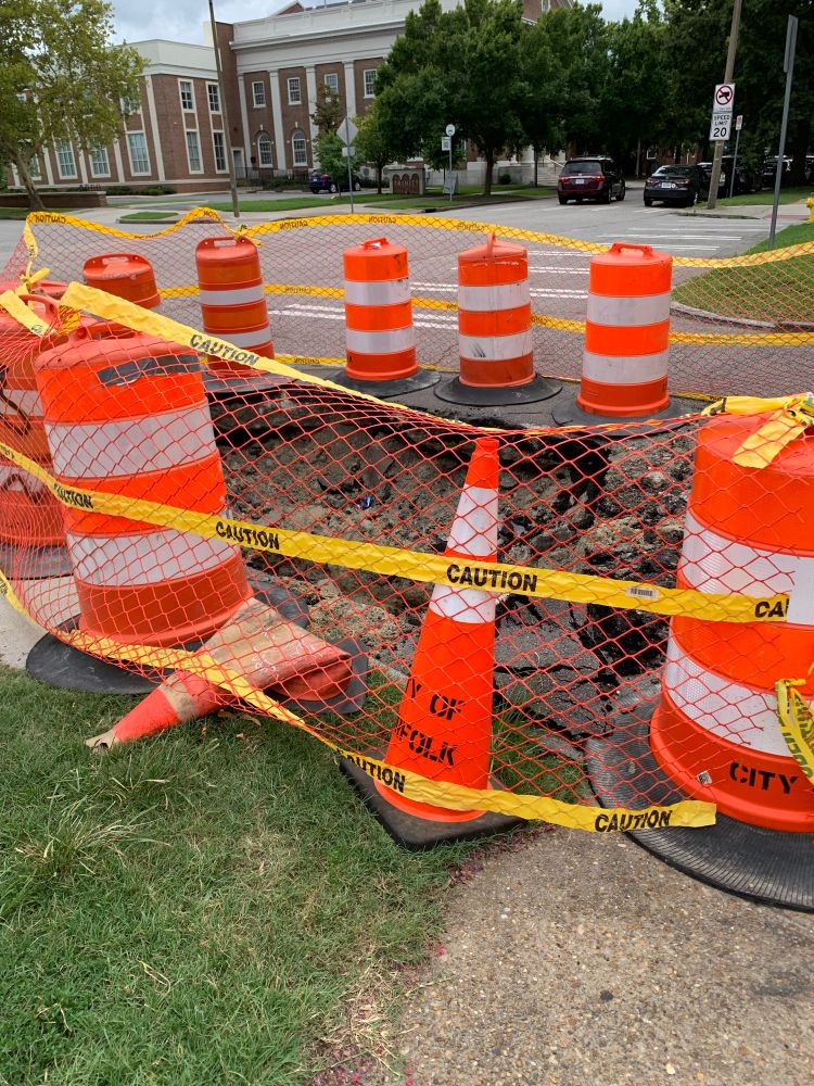 A sink hole almost big enough to fit a mini cooper outside the entrance of a pizza restaurant, surrounded by safety cones and hazard netting 