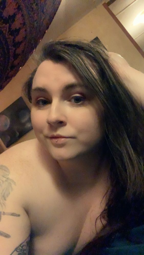 Trans girl laying on a bed with her head resting on her hand. She doesn’t appear to have any clothes on, but you can’t see anything to know for sure. 