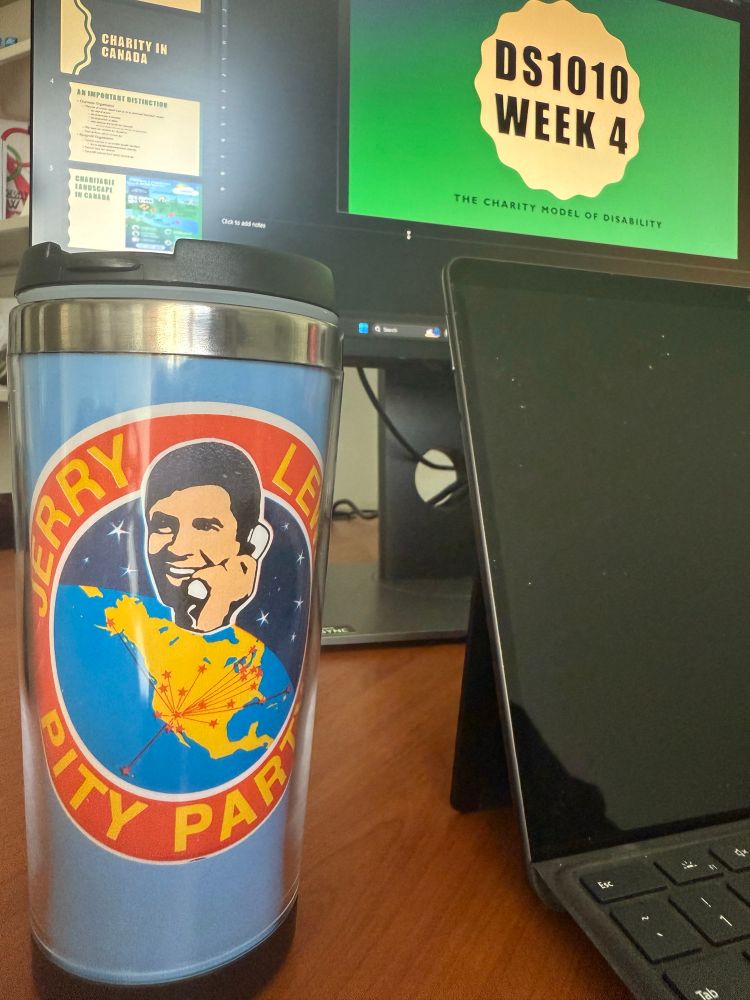 Tea mug with a “Jerry Lewis Pity Party” logo sitting before a computer screen with lecture slide titled “DS1010 Week 4 — The Charity Model of Disability”