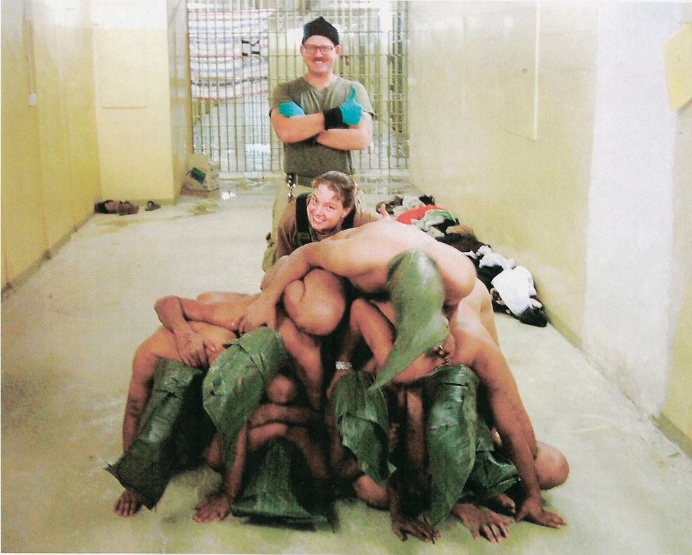 U.S. military posing with prisoners at Abu Ghraib in Iraq. 