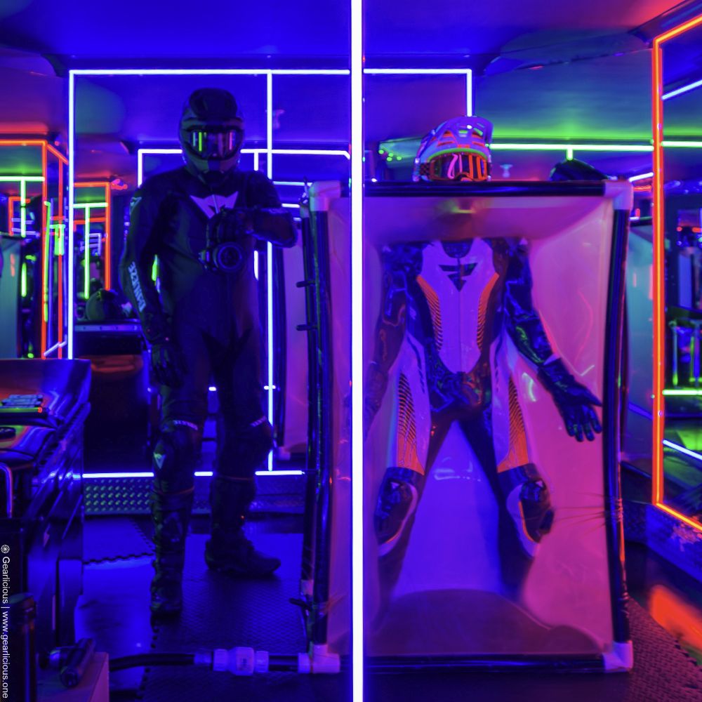 Two bikers, one in a Dainese black leather suit and helmet, taking the photo, and another sealed in a vacuum tower in a Shima leather suit with helmet exposed.
