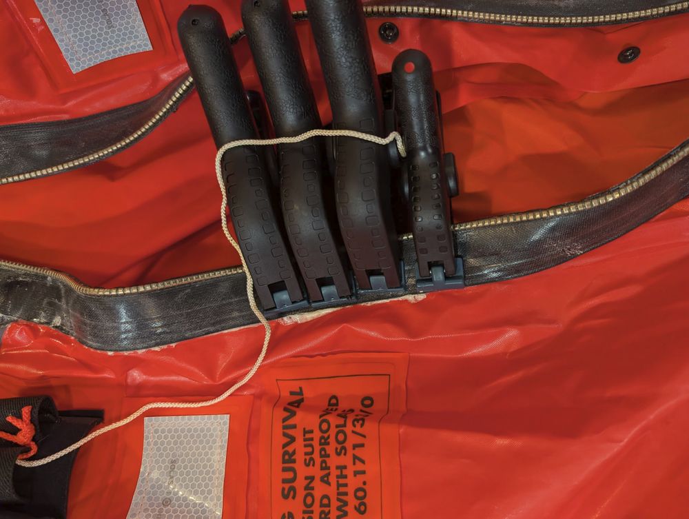 Four spring-loaded clamps holding a drysuit zipper to glue to a Mustang Ocean Commander survival suit.