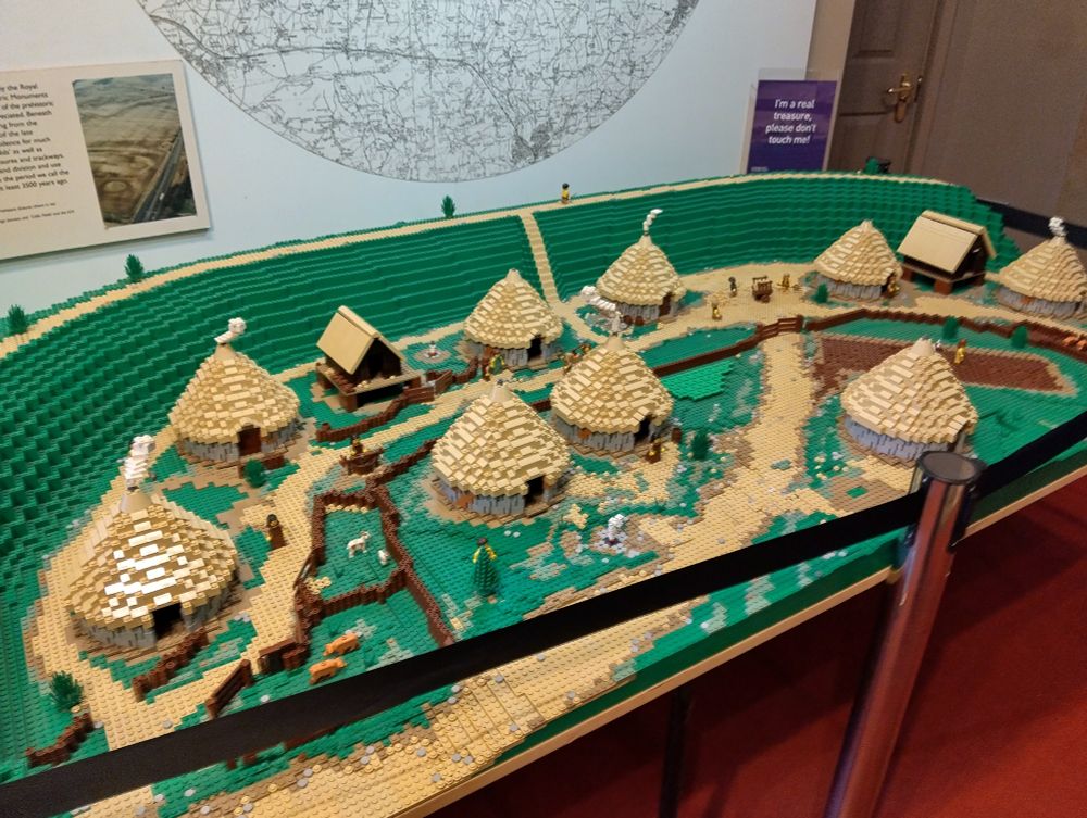 A diorama of 9 roundhouses inside a banked enclosure made entirely of Lego. Representing a view of Danebury Hill Fort from the Iron Age