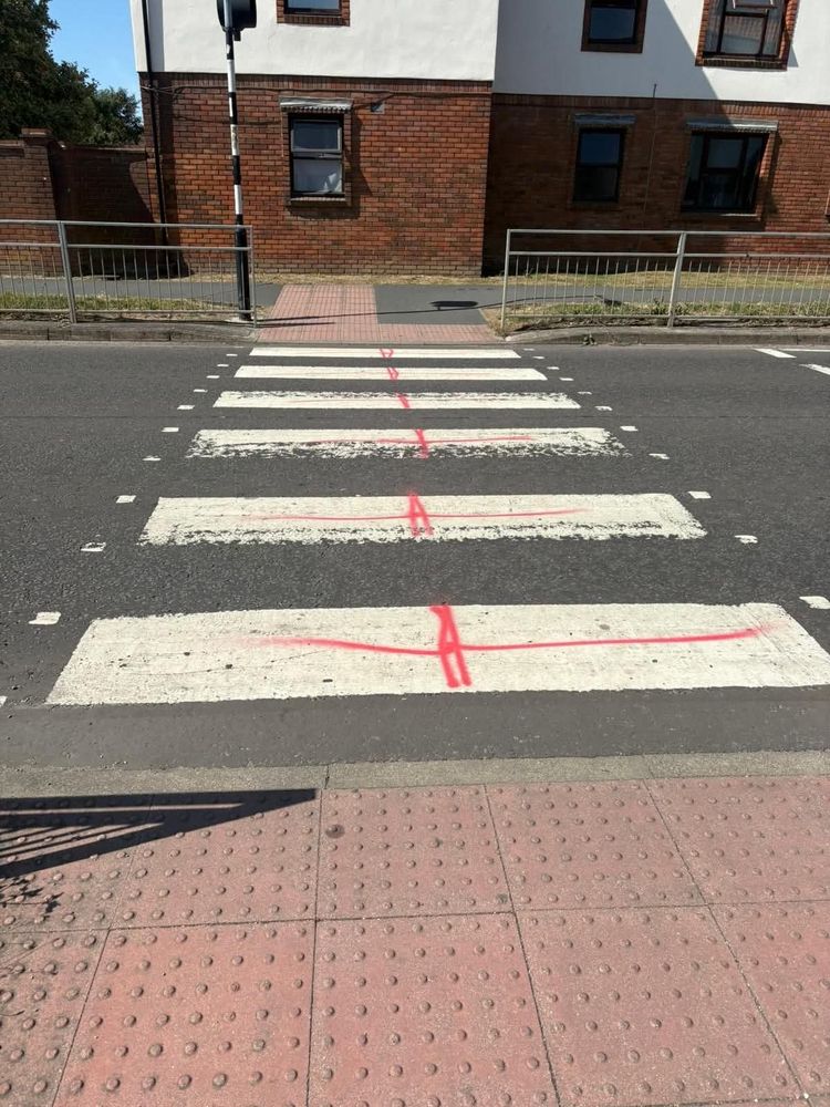 Zebra crossing with very very badly spray painted red lines painted on the white parts, presumably to emulated the England flag