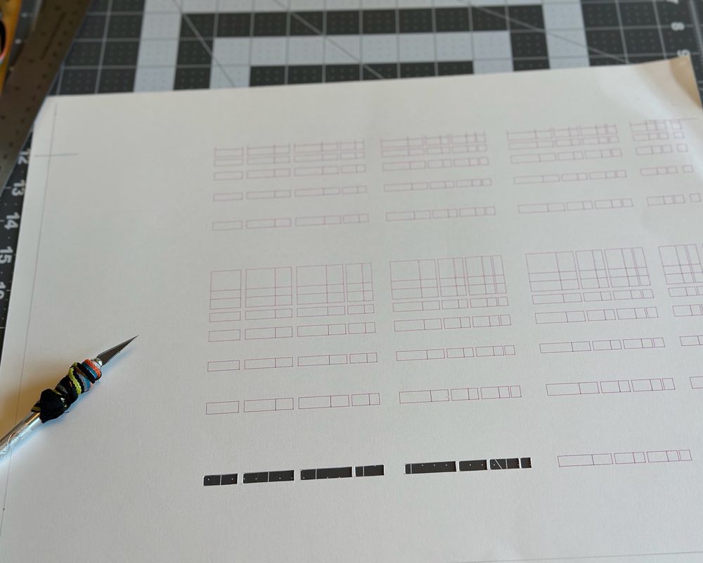 A knife sitting on a piece of paper that has a pattern printed on it. On row of the pattern has been cut out of the paper with the knife.