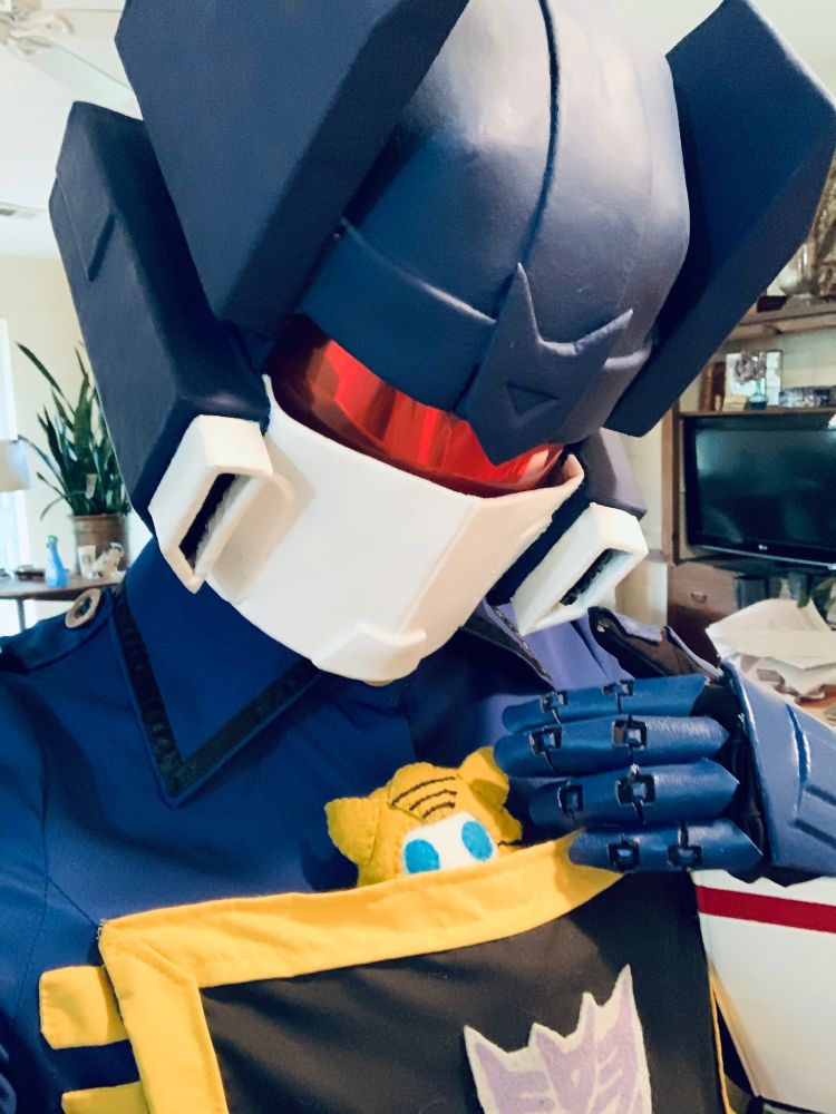 Soundwave gazes down at a yellow trimmed pocket on her chest where a plushie of Bumblebee is peeking out.