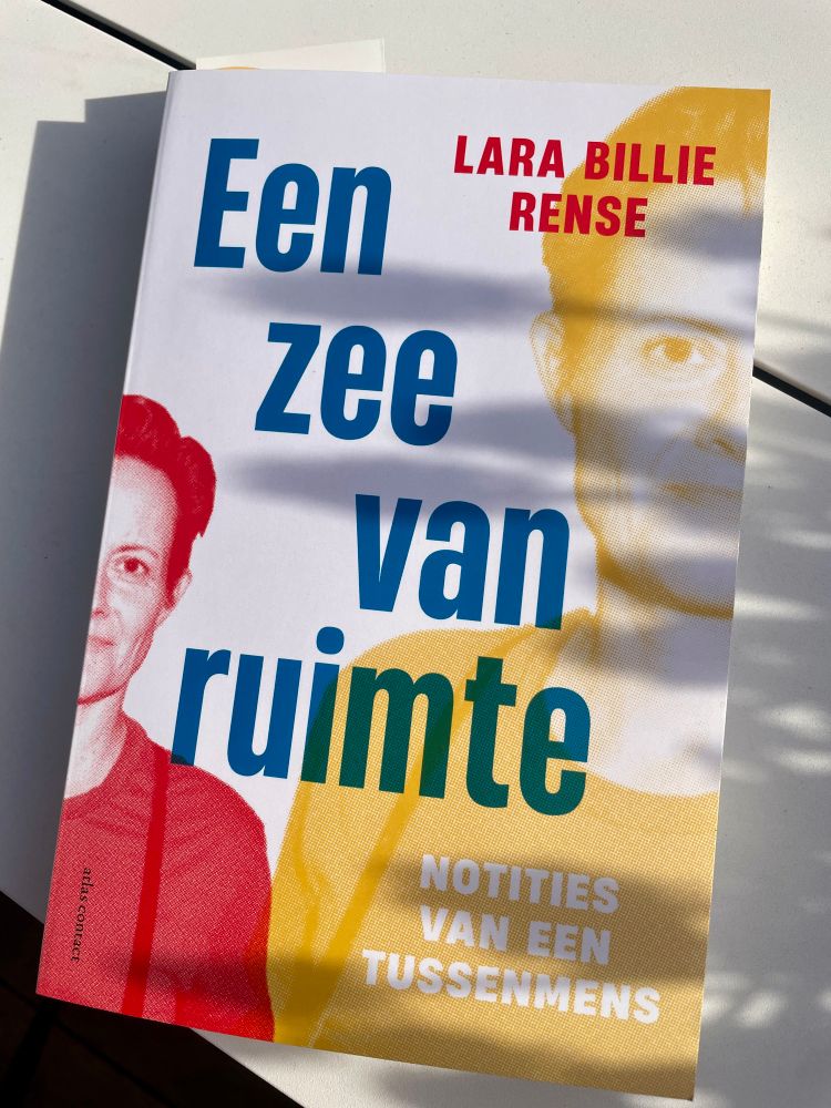 De voorkant van het boek “Een zee van ruimte” van Lara Billie Rense. Op de voorkant staat diens gezicht tweemaal half afgebeeld, links in duotoon rood en rechts in duotoon geel. Rechts bovenin staat in rode letters de naam van de auteur. De titel van het boek staat in blauwe, dik gedrukte letters in het midden, één woord per regel. De ondertitel leest “Notities van een tussenmens” en is wit, tegen de gele achtergrond van het rechter portret. Het boek ligt op een witte tuintafel en de schaduw van blauwe druifjes (de bloemen, niet de eetbare variant) is zichtbaar.