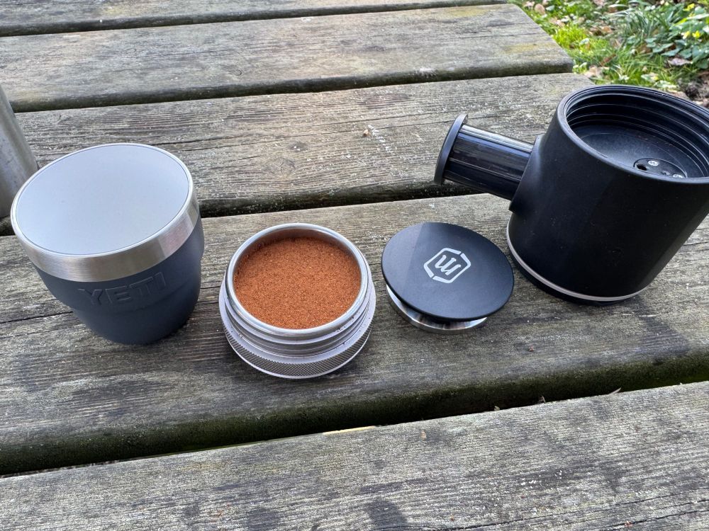 A close-up shot of a picnic table with a Yeti Espresso cup, a Picoexpress portafilter loaded with espresso, tamper and pressure chamber, ready to go. 