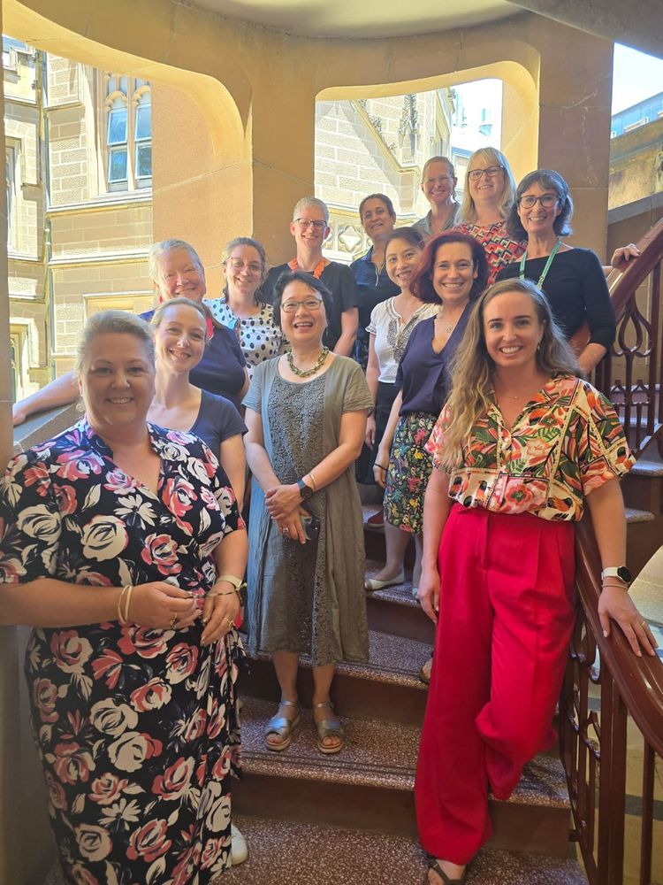 Speech pathologists standing on a spiral staircase with a sandstone building outside 