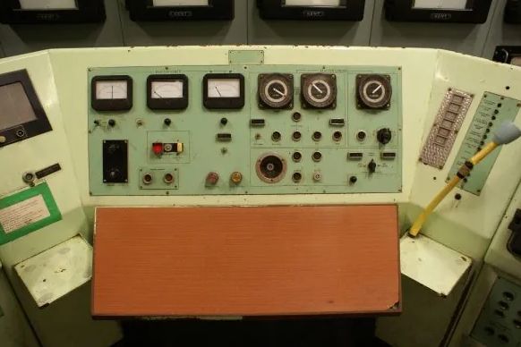 A 16mm film still of a control panel from within Dounreay Atomic Research Establishment - black buttons and dials on a green enamel panel.