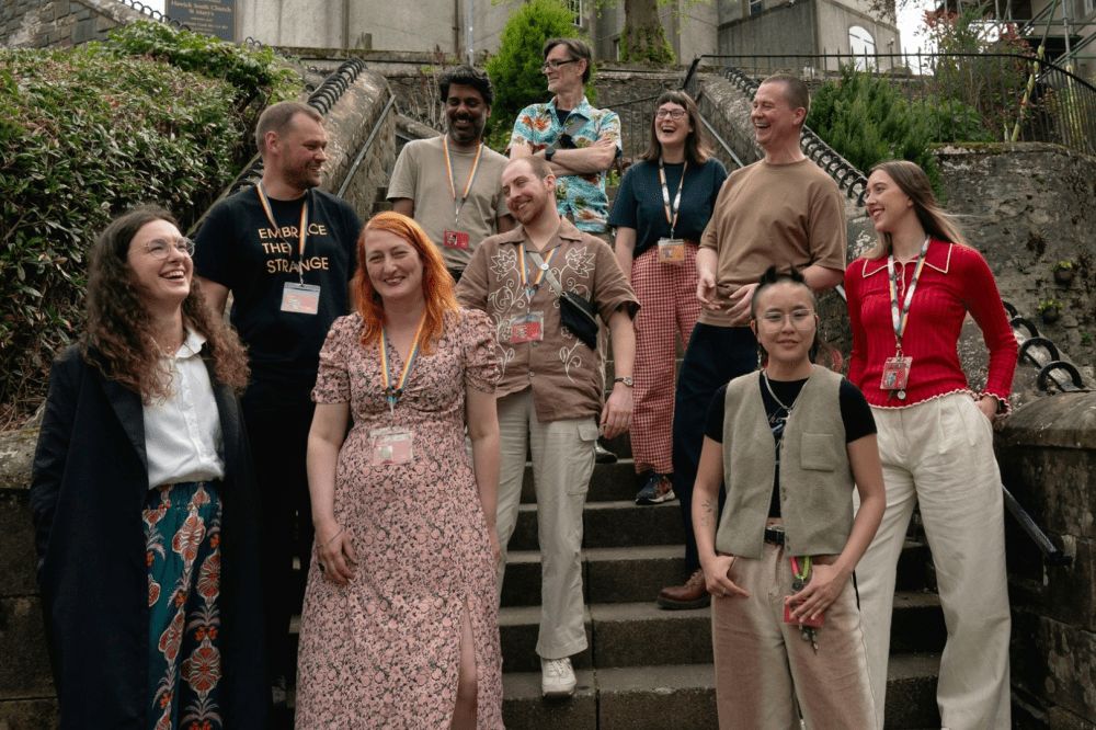 A group of people in colourful outfits gather on steps outdoors, looking cheerful and friendly
