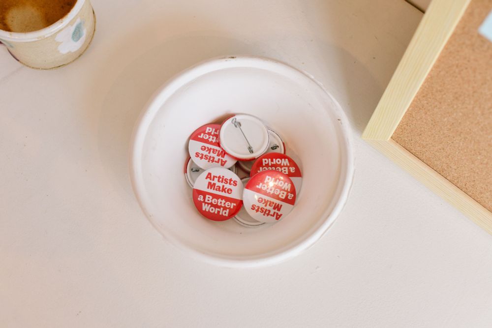 aerial shot of a bowl on a table, holding a number of red and white badges reading 'Artists Make a Better World'