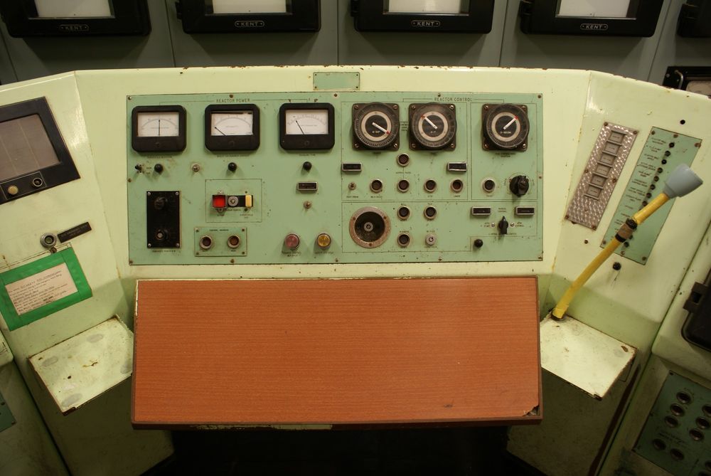 A 16mm film still of a control panel from within Dounreay Atomic Research Establishment - black buttons and dials on a green enamel panel.