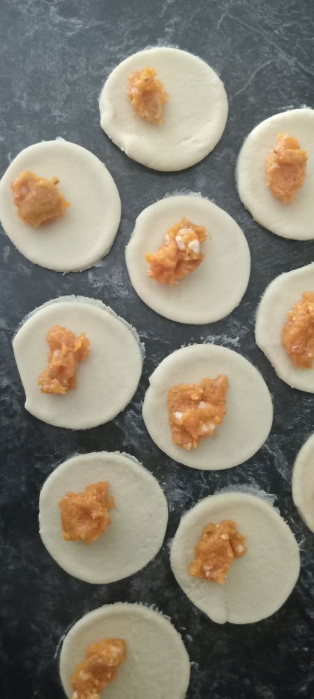 Orange dabs of pumpkin filling on white pasta on a black countertop.