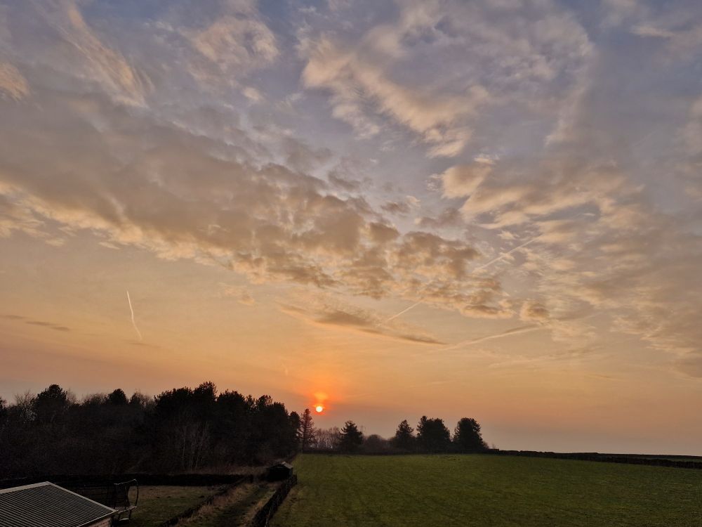Sunrise over field, orange at the bottom where the sun appears and blue sky with clouds 