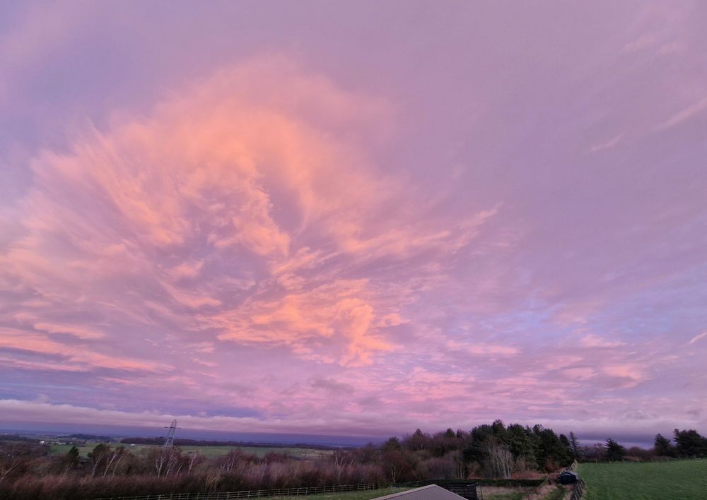 Pink, purple sunset sky with clouds spreading out like an explosion, over a field and forest. Sheffield, Peak District 