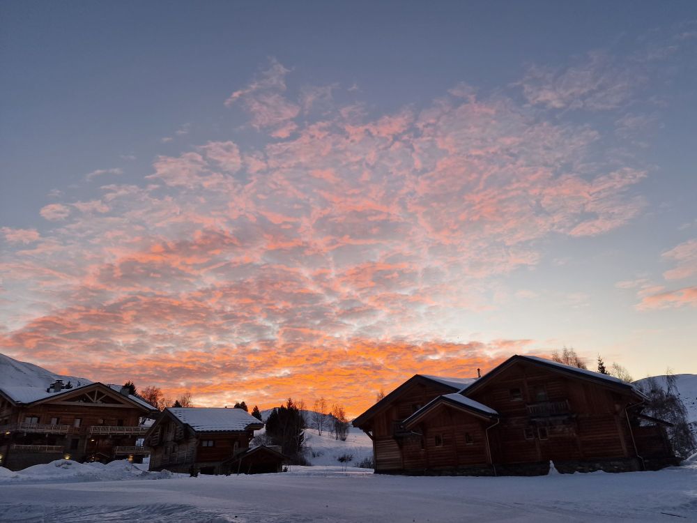 Orange/peach sunrise clouds in background with ski piste and snowy chalets in foreground 
