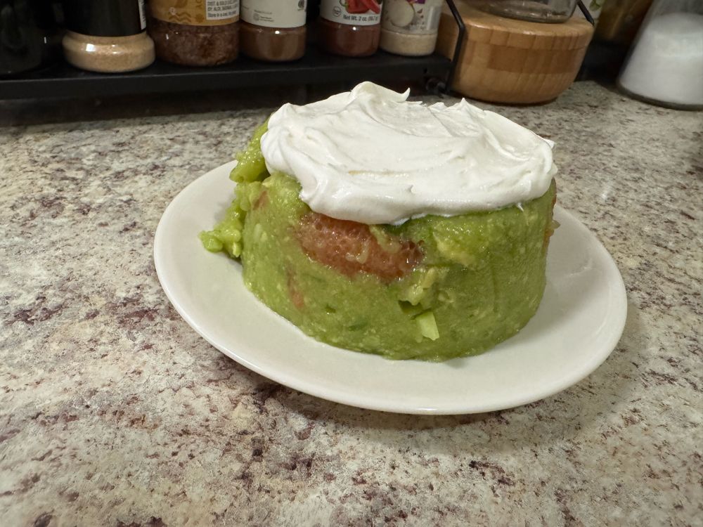 Picture of a de-molded bowl of this horrible salad atop a saucer. It is an Incredible Hulk green color with a slice or reddish orange grapefruit protruding on the side and it is topped with a white creamy mixture. 