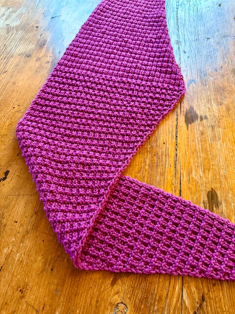 Textured handknit shawl laid out on wooden table. 