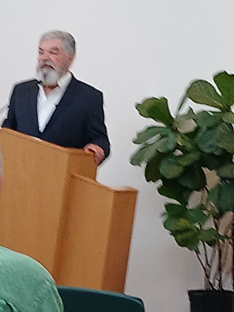 Marcel Rivera 80 years old. Blue jacket with white shirt. Has a Grey beard and Grey hair. Standing behind a letter at Universalist Unitarian Church in New orleans. 