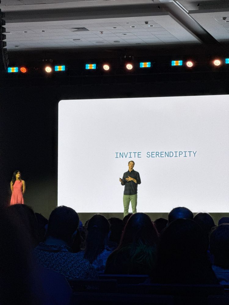 A slide saying "invite serendipity" projected behind two speakers 
