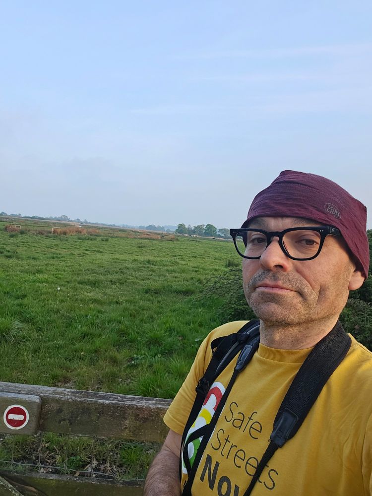 A runner in yellow shirt & purple hat, with Exminster Marshes in the background 