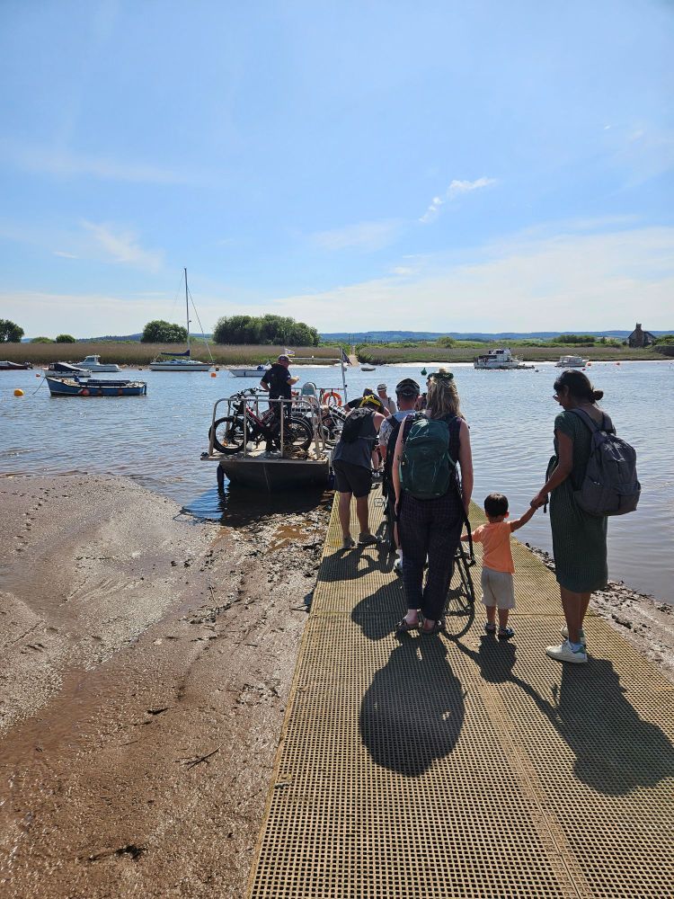 Families wait on slipway to board ferry. The sky is blue.