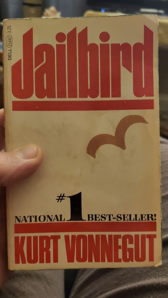 Holding a paperback copy of Jailbird by, Kurt Vonnegut.