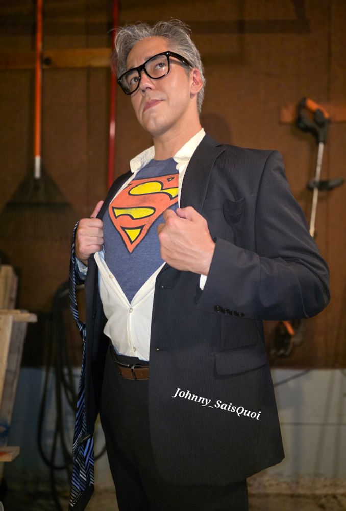Johnny wearing a navy suit and button up shirt, pulled apart to reveal the Superman logo