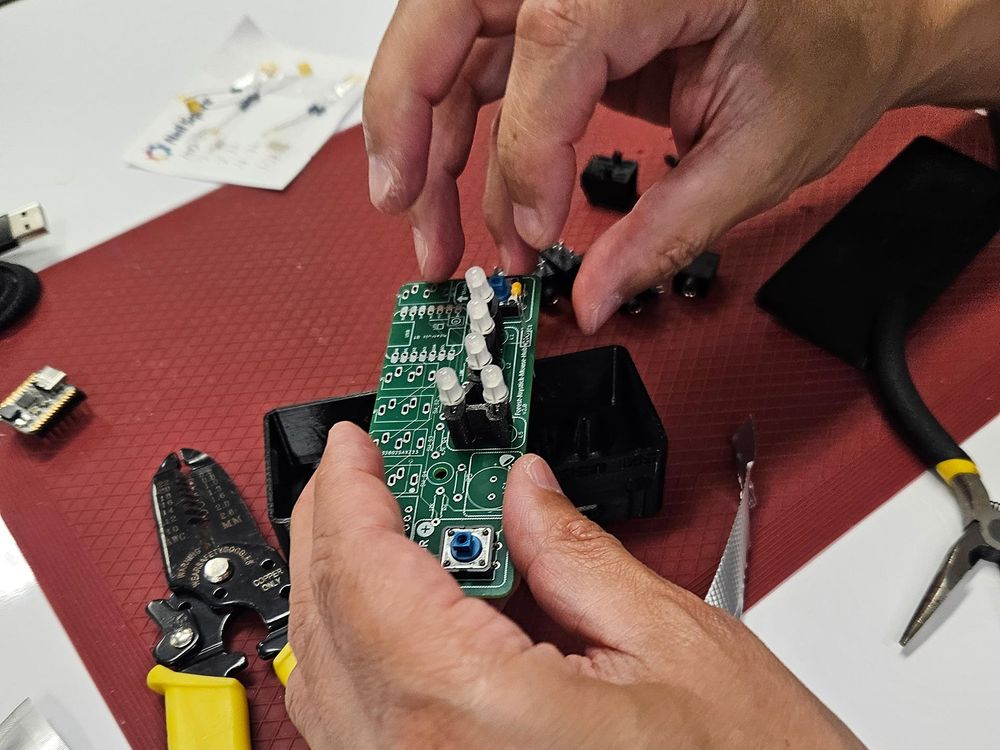 Hands hold a device over a mat. Tools are scattered around.