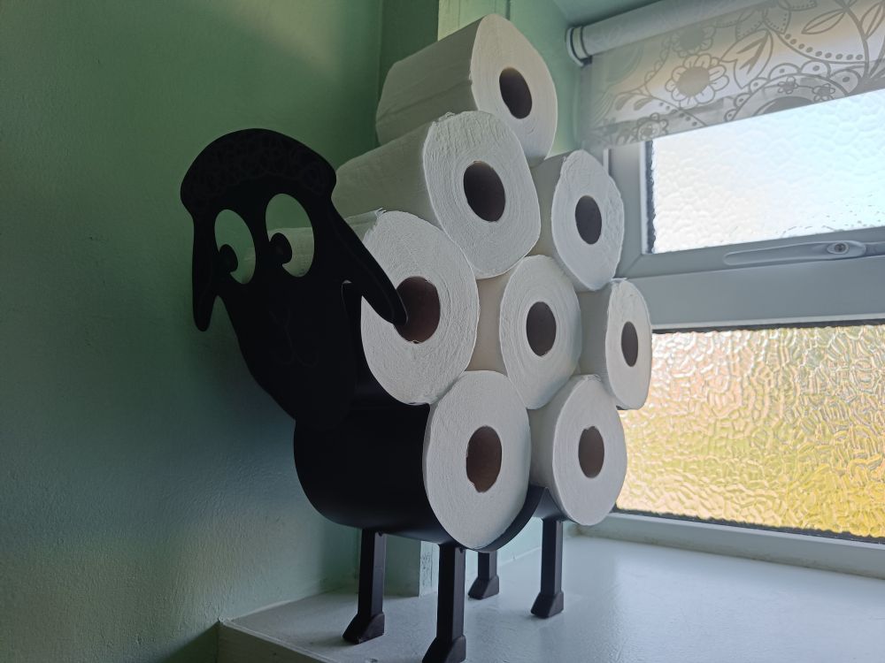 A metal sheep on a windowsill. The sheep has 8 toilet rolls stacked on it's back, to represent the wool.
