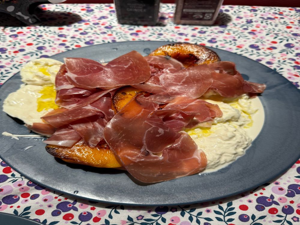 Grilled peach, burrata and prosciutto drizzled with olive oil on a blue rimmed plate. 