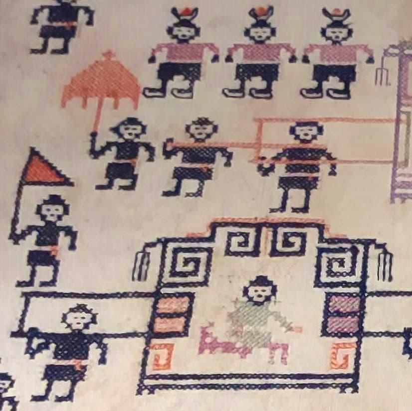 Closeup of Chinese embroidered pillow cover. The stitching (looking very much like low-resolution pixel art from 1980's games) shows simple figures in black, some carrying red umbrellas or flags as other figures carrying royal figures in ornate sedan chairs.
