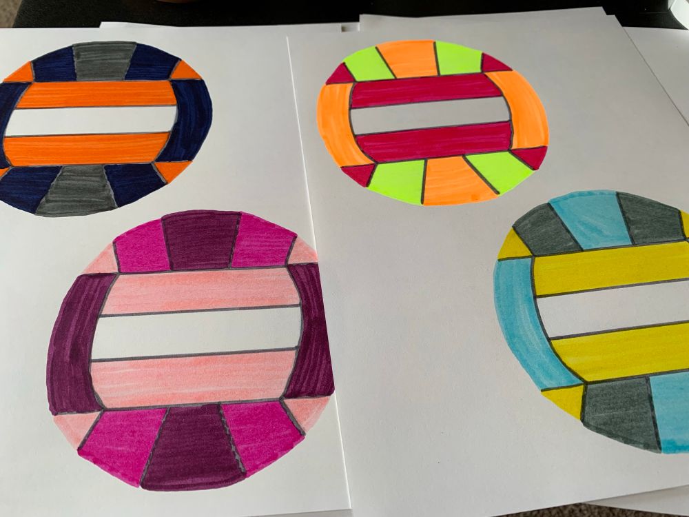 Two white pieces of paper with a drawing of two volleyballs on each page. all the volleyballs are colored in with markers and bright colors.