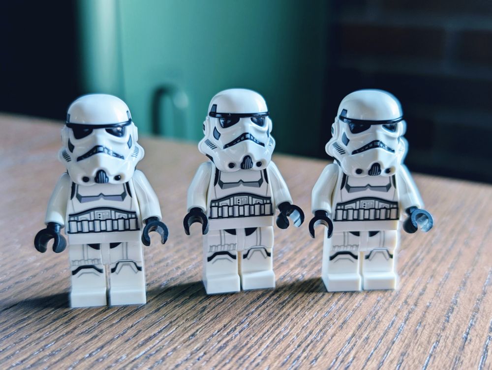 A trio of Star Wars Lego stormtroopers standing side by side on a desk.