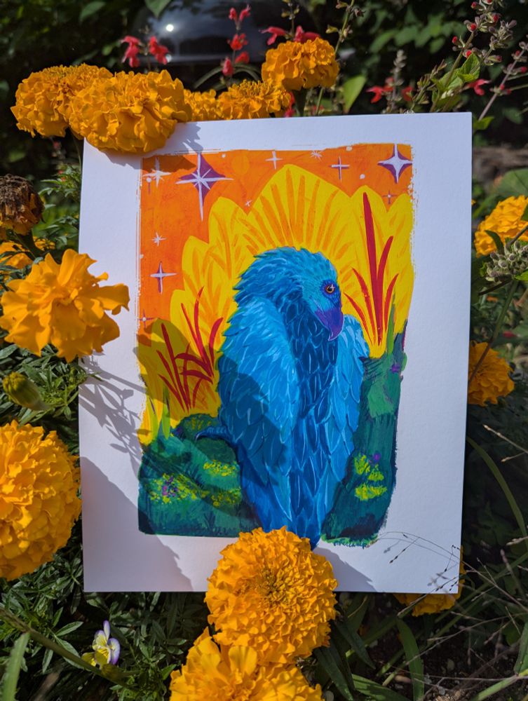 An art print of a vibrant blue bird against gold and orange and green backgrounds is sitting among marigolds and grass