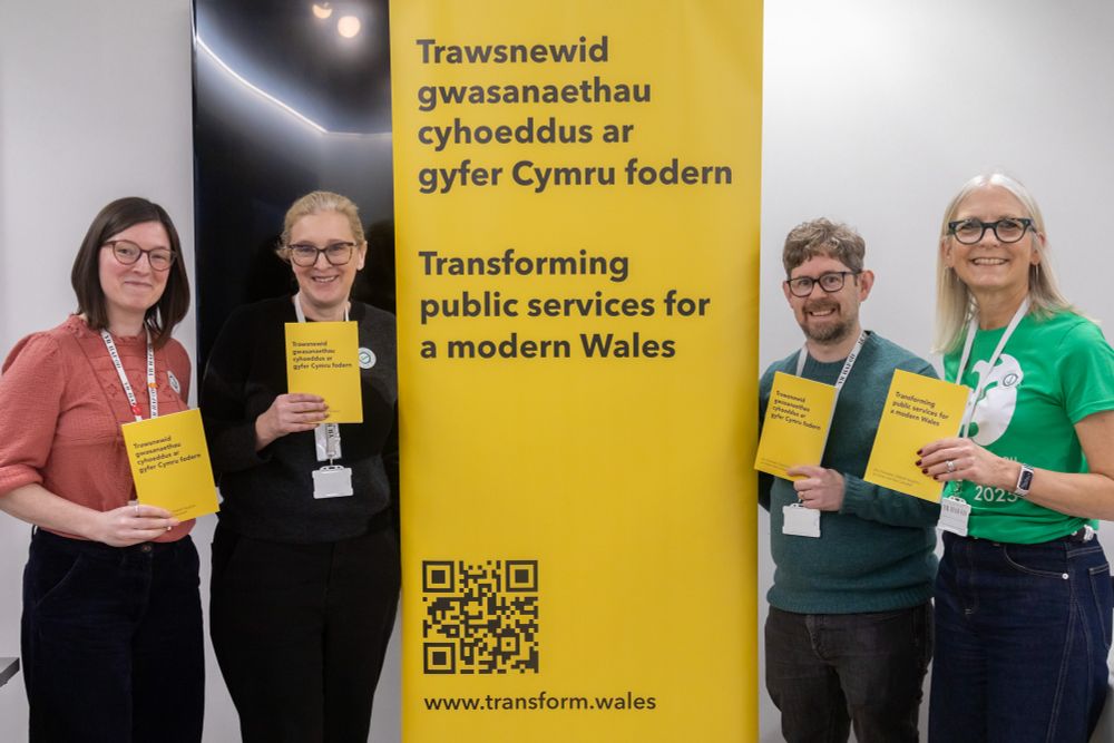 The Transform Wales team holding copies of the Transform Wales report next to yellow banner that says "Transforming public services for a modern Wales"