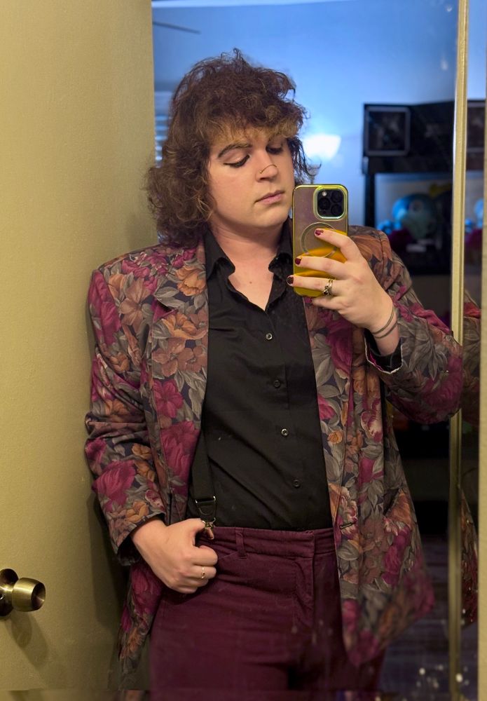 A mirror selfie of fae in a burgundy and floral print jacket with a black button up shirt