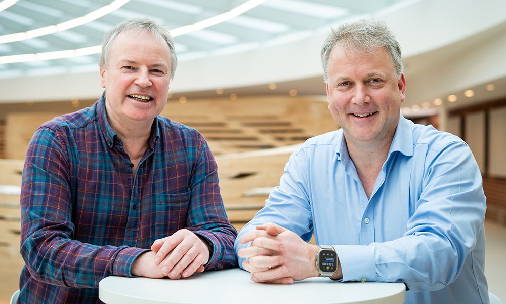 Two men standing at a table, smiling to camera.