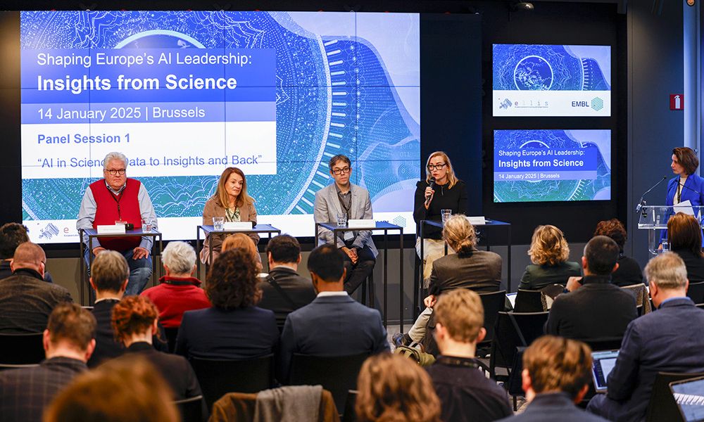 Four panelists are talking at a stage, observed by the audience. The slide behind them displays text:  "Shaping Europe's AI Leadership: Insights from Science; 14 January 2025 | Brussels; Panel Session 1: AI in Science: Data to Insights and Back".
