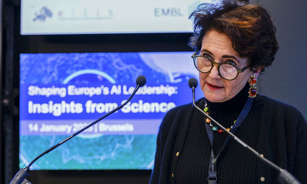 EMBL Director General Edith Heard is speaking to microphones. The slide behind her displays text:  "Shaping Europe's AI Leadership: Insights from Science; 14 January 2025 | Brussels".