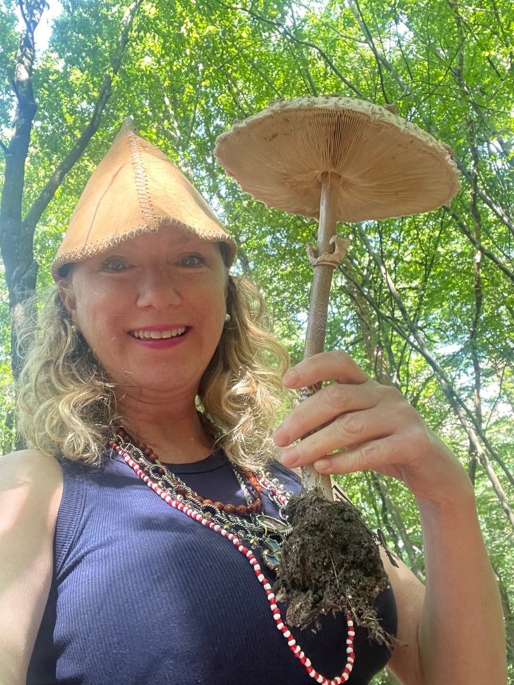 Me in a gnome hat holding a parasol mushroom in the woods 