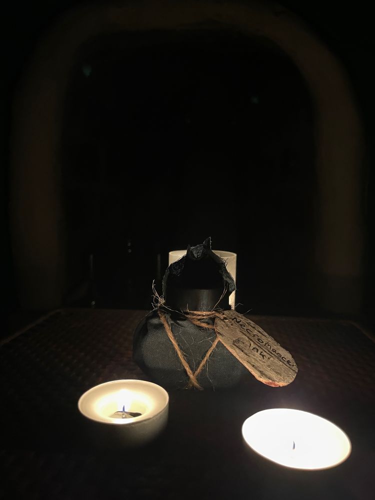 A black cloth wrapped ink bottle surrounded by 3 lit candles