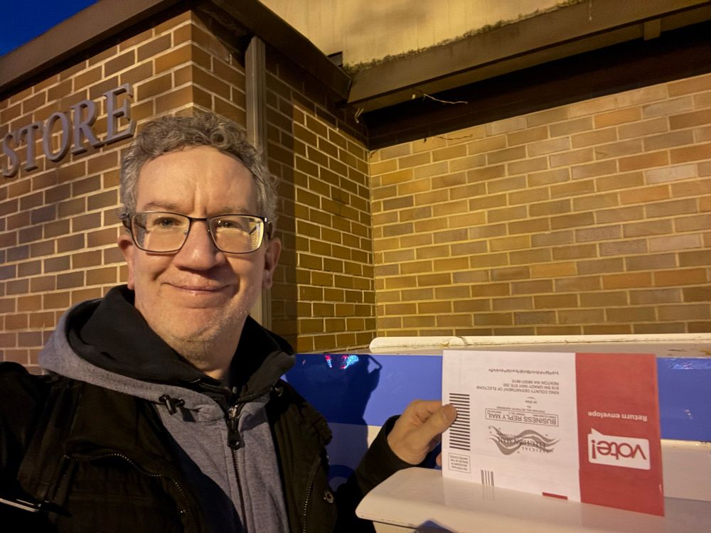 Selfie photo at the ballot dropbox in North Queen Anne, Seattle, about to put my ballot in the box. Kind of smiling stiffly, not one of my better selfies. Also I’m holding the ballot envelope upside down. The thing is, I took a second photo to try to get a better smile and both failed in that and failed to notice I was (still) holding the envelope upside down, so this is the best you get. Anyhow what matters is, I VOTED, YOU SHOULD TOO.
