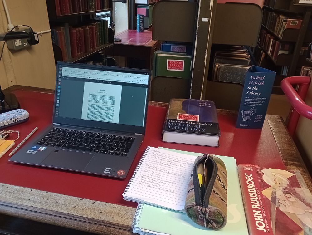 Desk with laptop, books and notebooks. Library bookstacks can be seen behind the desk 