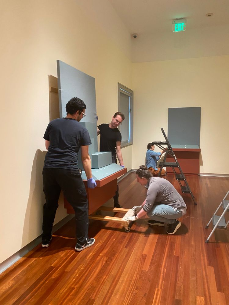 Three people disassemble a display case.