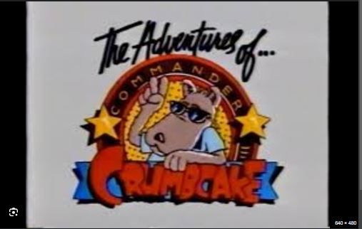 Cartoon logo of a dog (possibly a schnauzer) wearing sun glasses and making a peace sign. The logo reads: "The adventures of Commander Crumbcake"