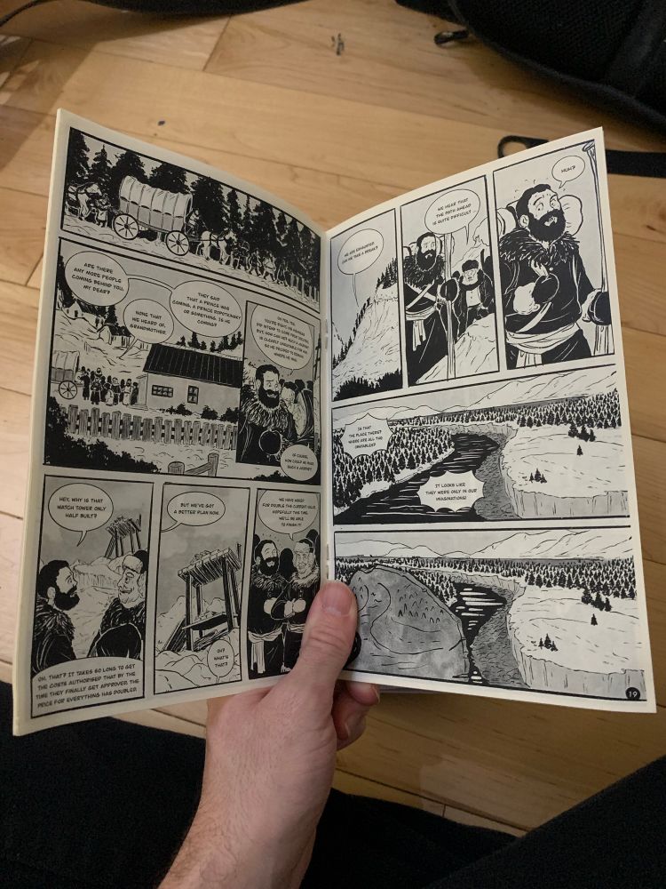 A hand showing an open comic with black and white pages inside.